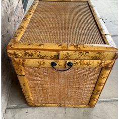 an old wooden trunk with wicker handles sitting on the ground next to a brick wall