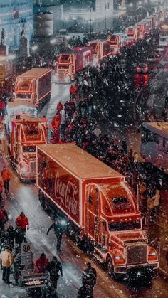 a large group of trucks driving down a snow covered street next to tall buildings and traffic lights