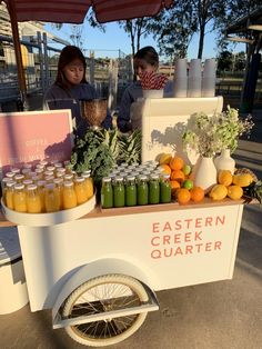 two women standing behind a cart with drinks on it and oranges in mason jars