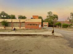 a person riding a skateboard down a dirt road next to a building and trees