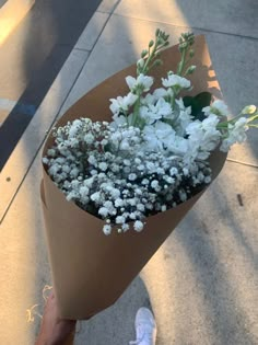 a bouquet of white flowers is wrapped in brown paper and placed on the sidewalk next to someone's feet