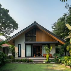 This minimalist bungalow showcases a gabled roof and a sleek white exterior with warm wood accents. Large glass doors and windows flood the interior with natural light and open to a beautifully landscaped garden. The front yard features tropical plants and a manicured lawn, creating a serene ambiance. With its clean lines and modern design, this bungalow harmoniously blends simplicity, functionality, and a strong connection to nature. Perfect for those who love minimalist architecture. Minimalist Modern Tropical House, Modern House With Plants Exterior, Bungalow Tropical House, Gable Roof House Design, Modern Tropical House Design Exterior, Tropical Houses Exterior, Tropical Exterior House Design, Tropical Roof Design, Tropical Bungalow House Design