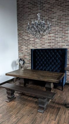 a table and bench in front of a brick wall with a chandelier hanging from the ceiling