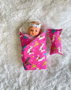 a baby doll in a pink bag on a white blanket with pillows and blankets around it