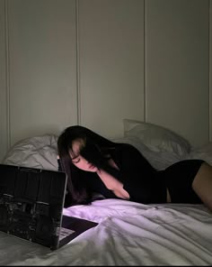 a woman laying in bed with her head on the pillow while using a laptop computer