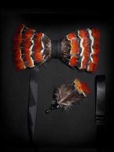 A luxurious feather bow tie featuring bold orange and black stripes with white accents, accompanied by a matching lapel pin, neatly arranged in a gift box.