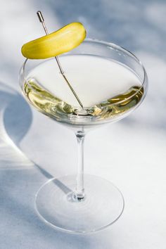 a glass filled with white wine and a yellow pickle on the top of it