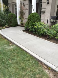 a driveway with grass and bushes in front of a house