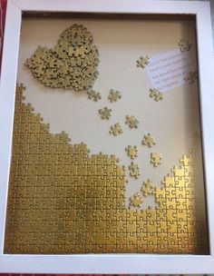 a white frame with gold puzzle pieces in the shape of a heart on top of it