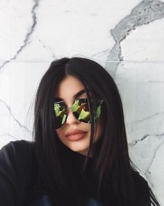 a woman with sunglasses on her head and long black hair is posing in front of a marble wall