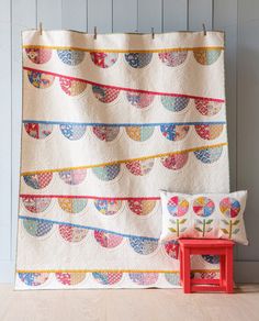 a quilted wall hanging next to a red chair and small table with a pillow on it