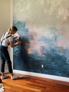 a woman painting a wall with blue and pink paint