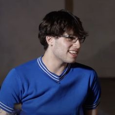 a man wearing glasses and a blue shirt smiles at something he is holding in his hand