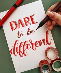 a hand holding a pen over a piece of paper with the words dare to be different written on it