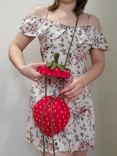 a woman holding two strawberries in one hand and the other with a flower on it