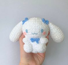 a hand holding a white stuffed animal with blue eyes and a bow on it's head