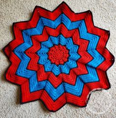 a red, blue and white crocheted blanket laying on the floor next to a wall