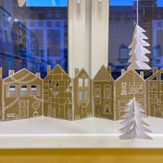 a paper cut out of houses and trees on a window sill with buildings in the background