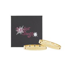 two gold bracelets sitting next to each other in front of a black card with the words taylor swift on it