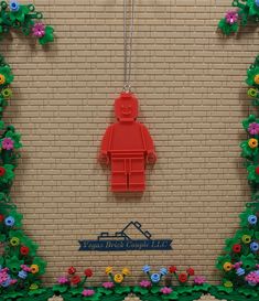 there is a red lego man hanging from a brick wall with flowers on the side