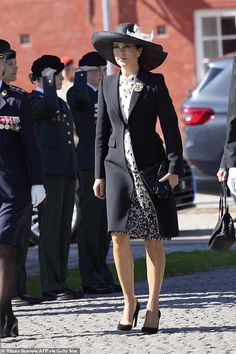 a woman in a dress and hat walks down the street with other people behind her