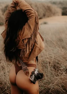 a woman wearing a brown jacket and tie standing in tall grass with her back to the camera