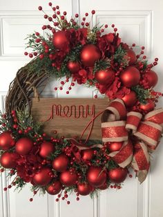 a christmas wreath with the word merry written on it and red ornaments hanging from the front door