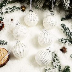 white christmas ornaments in the snow surrounded by pine cones