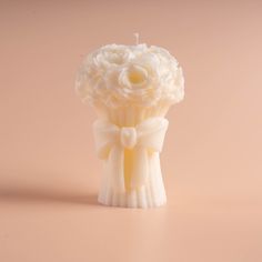 a small white vase with flowers in it sitting on a table next to a candle