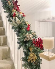 a christmas garland with pine cones and red berries is on the banister next to stairs