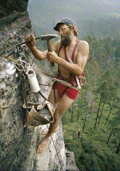 a shirtless man climbing up the side of a cliff with an ax in his hand