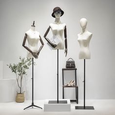 three mannequins with hats and purses on stands in front of a white wall