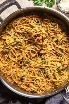 pasta in a pan with parsley and garlic on the side, ready to be eaten