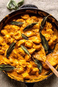 a skillet filled with pasta and sages on top of a table next to a wooden spoon