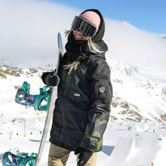 a woman standing on top of a snow covered slope holding a snowboard in her hand