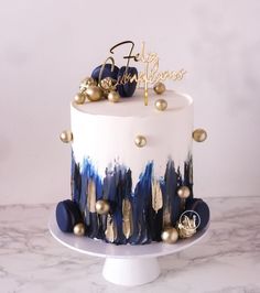 a white and blue cake with gold decorations on it's top, sitting on a marble table