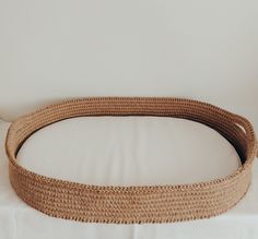 a round wicker bed with white linens on the bottom and sides, in front of a plain wall