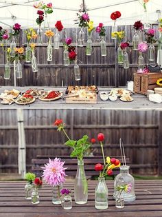 several vases filled with flowers sitting on top of a wooden table covered in food