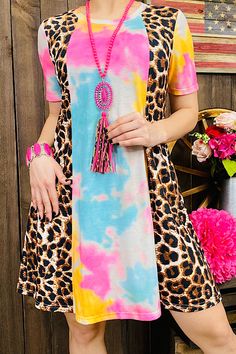 a woman standing in front of a wooden wall wearing a tie dye dress and necklace