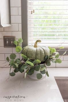 a white bowl filled with green plants on top of a counter next to a window