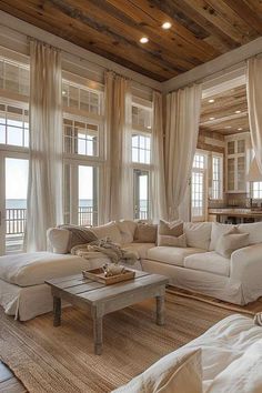 a living room filled with lots of white furniture next to large window covered in curtains