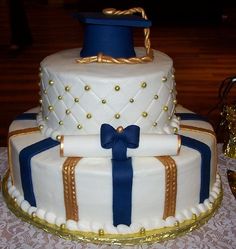 a three tiered cake with blue ribbon and gold trimmings on a table