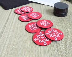 six red buttons sitting on top of a table next to a pile of black coins