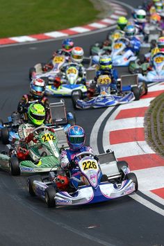 a group of people racing go kart cars on a race track with grass in the background