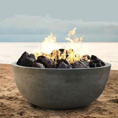 a fire pit sitting on top of a sandy beach next to the ocean with rocks in it