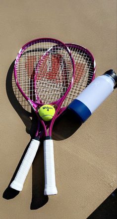 two tennis racquets are laying on the ground next to a bottle of water