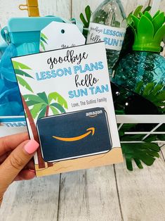 someone holding up an amazon gift card in front of some plants and other things on the table