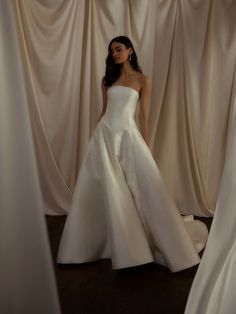 a woman in a white wedding dress standing next to some draperies with her hands on her hips