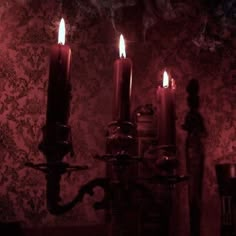 three lit candles are sitting on a table in front of a wallpapered wall