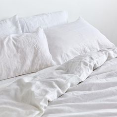 an unmade bed with white sheets and pillows